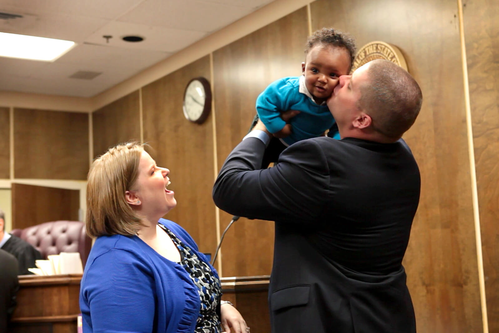 man holding up and kissing small child in court