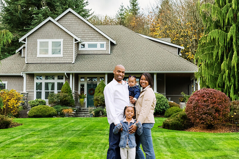 Portrait of a happy young African American family standing in front of their American suburban home.