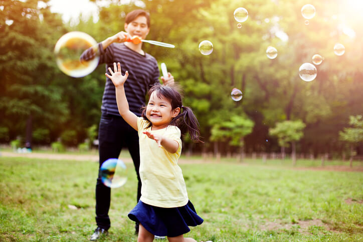 Father and daughter having fun in park with Soap Bubbles