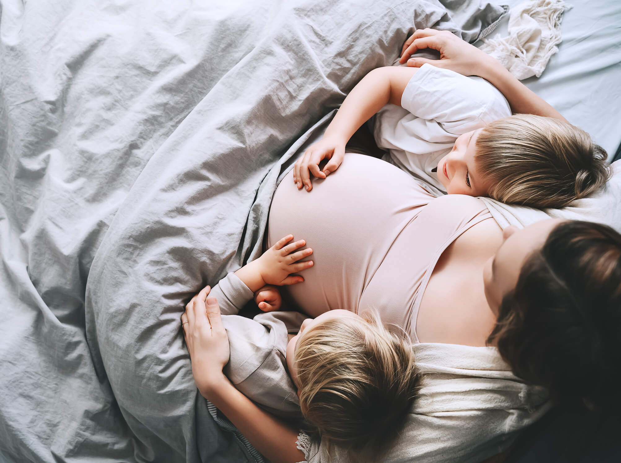 Pregnant woman with her children relaxing in bed. Loving mother and toddlers together at home.