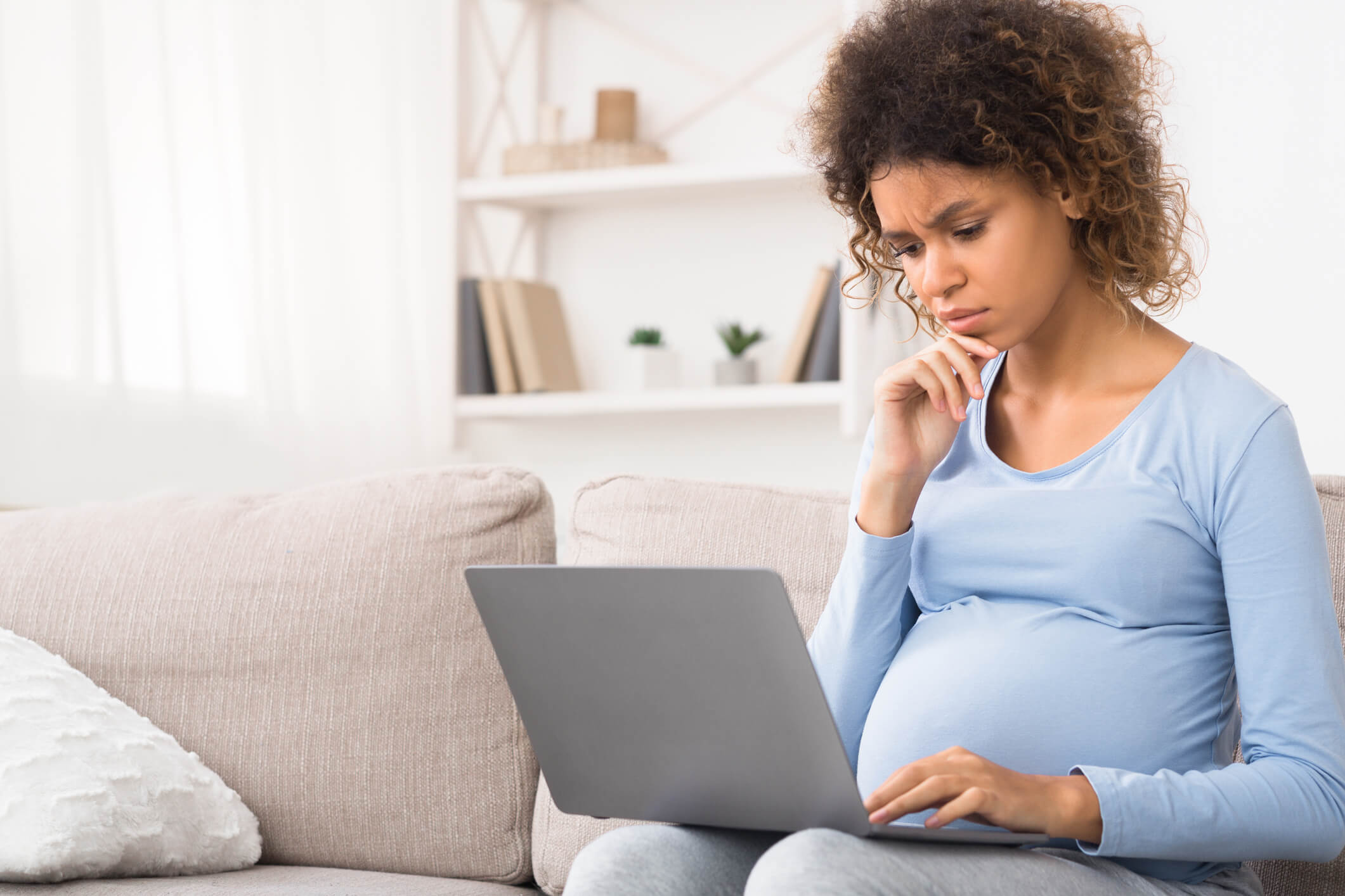 Confused pregnant woman looking at laptop for answers