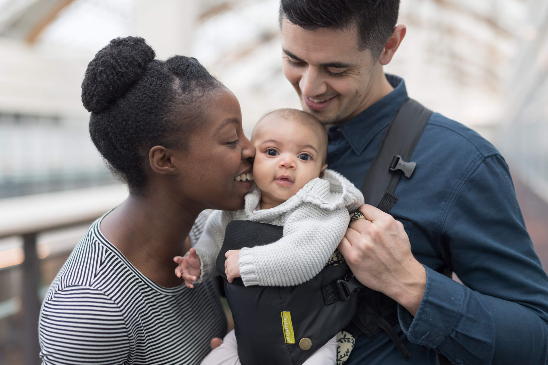 Affectionate multi-ethnic couple are shopping with their baby daughter who is riding in a baby carrier