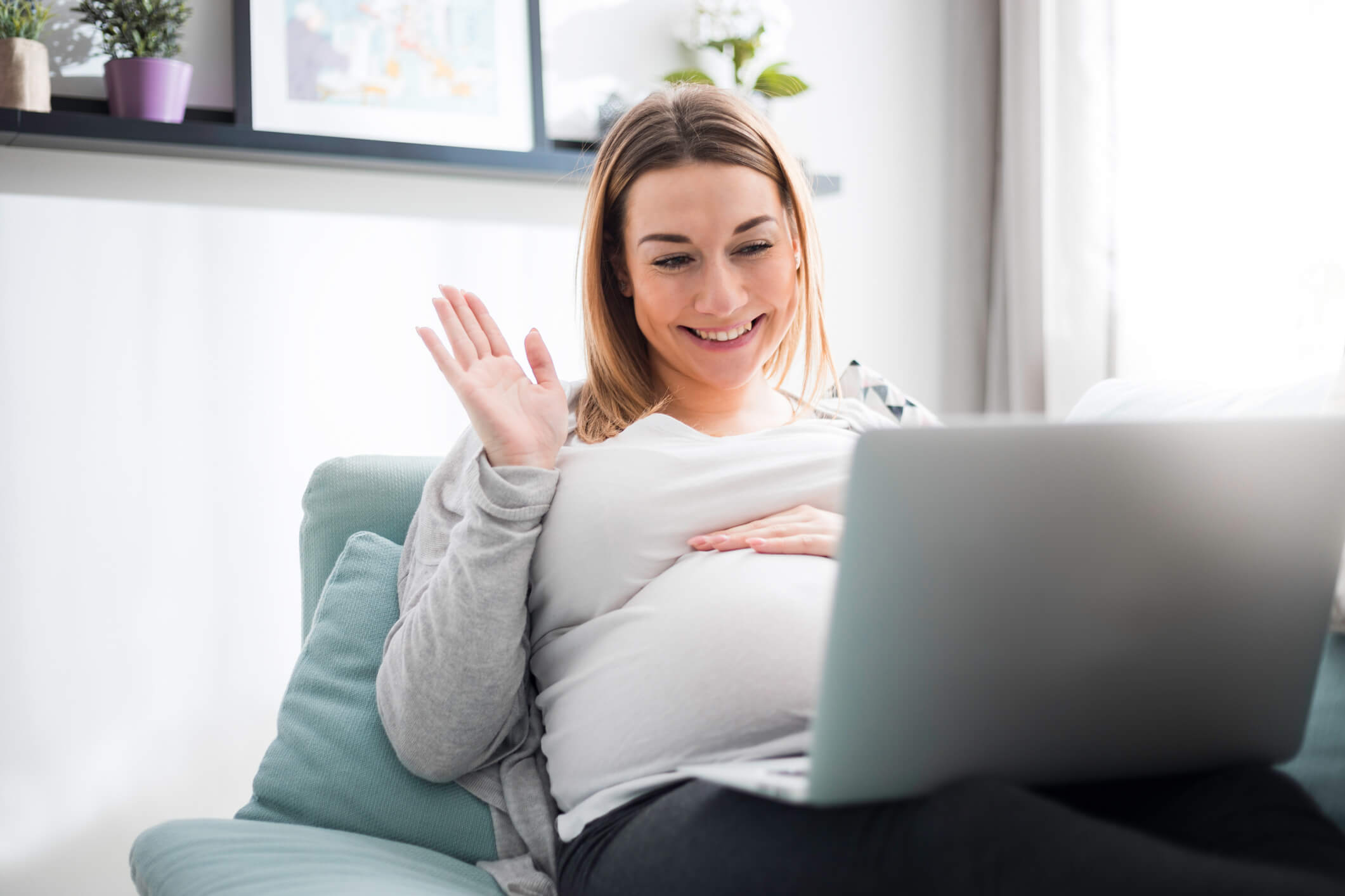 Pregnant woman video chatting with family on laptop waving hand to screen